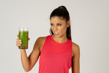 Beautiful young sport woman tired of diet holding green smoothie in dislike