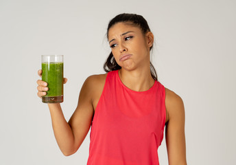 Beautiful young sport woman tired of diet holding green smoothie in dislike