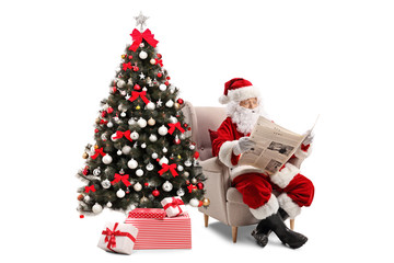 Surprised Santa Claus sitting in an armchair and reading a newspaper