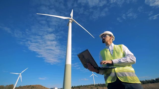 Functioning wind turbine towers and an energetics worker standing beside them with a laptop. Clean, eco-friendly energy concept.