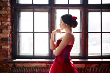 Portrait of a beautiful young woman dancer in a red dress near the window.