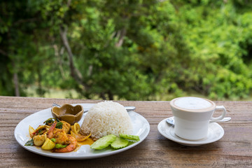 Stir-fried sea food with chili paste on Rice with latte coffee cup on wooden table