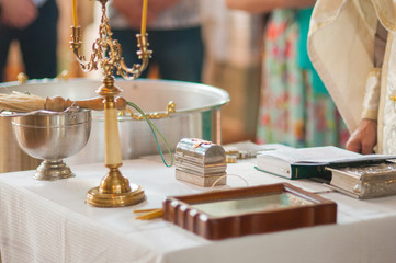 Religious items for a baptismal ceremony are arranged on an altar table in a church, featuring a candelabra, font, holy books, and an icon.