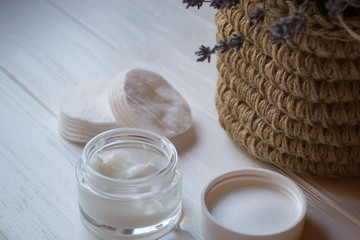 A jar with skin cream and lavender flowers on a white wooden background.