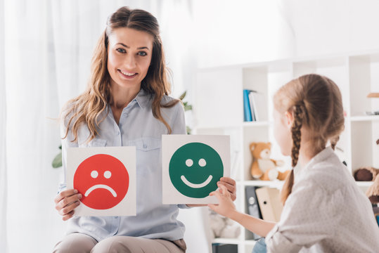 Smiling Psychologist Showing Happy And Sad Emotion Faces Cards To Child