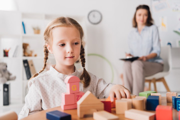 adorable little child playing with blocks while psychologist sitting blurred on background