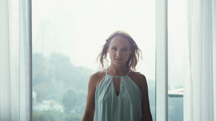 Portrait of an attractive businesswoman standing in front of windows in an office building smiles and looks at camera