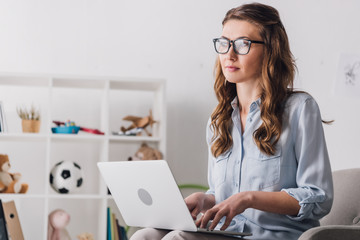 close-up portrait of child psychologist sitting in armchair with laptop and looking away