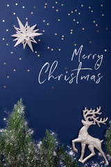 Holiday greeting card with inscription Merry Christmas. Christmas scene made of silver figurines of reindeer, star and evergreen branches on dark blue background. Christmas night concept.