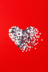 Broken heart made of silver confetti on red background. Valentine's day greeting card.