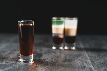 Bartender pours alcoholic drink into small glasses on bar. Colorful cocktails at the bar. Colorful shots at the club. Alcoholic drink in different colors. Nightlife scene. Shots at the bar table.
