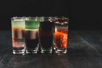 Set of alcoholic cocktails in shot glasses (shooters) on black wooden background