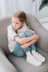 Fototapeta premium high angle view of lonely little child sitting in armchair and looking away
