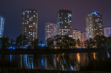 Fototapeta na wymiar Apartment buildings with glowing windows near the pond at night.