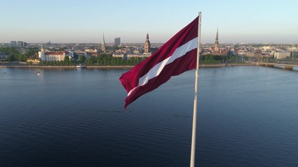 Aerial drone rising shot revealing Riga Old Town behind a large flag of Latvia