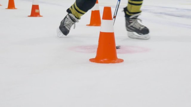 hockey training, player on skates with hockey stick leads puck past road cone on ice rink