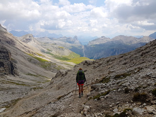 Hiker with backpack walking a stony path trail and holding rope on top of a mountain during trip in the alps