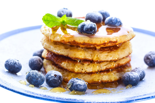 Pile of pancakes with blueberries sprinkled with icing sugar and poured on with honey
