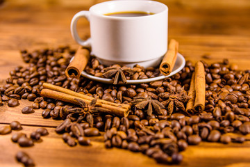 Cup of hot coffee, star anise, cinnamon sticks and scattered coffee beans on wooden table