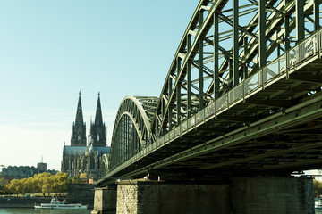 Obraz premium The Cologne Cathedral with Hohenzollern Bridge in the foreground on a bright sunny day. People are walking on the bridge