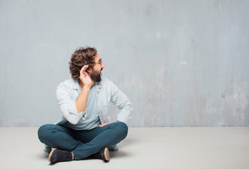 young cool bearded man sitting on the floor. grunge wall background