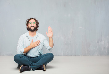 young cool bearded man sitting on the floor. grunge wall background