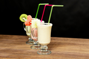 Smoothie still life on a wooden table. Black background. At the edges of the glasses are slices of kiwi, watermelon and pineapple.