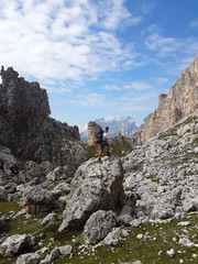 Hiker with backpack climbing a stony path trail and holding rope on top of a mountain during trip in the alps