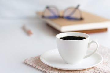 A cup of white coffee, pen, and books are placed on bright pink cloth.  The concept of relaxation with coffee in the morning.
