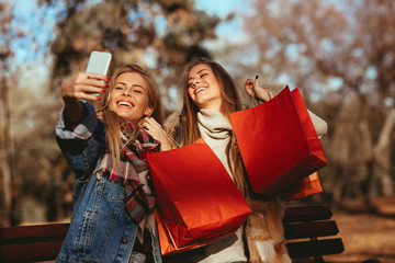 Two women friends taking a selfie in park after shopping