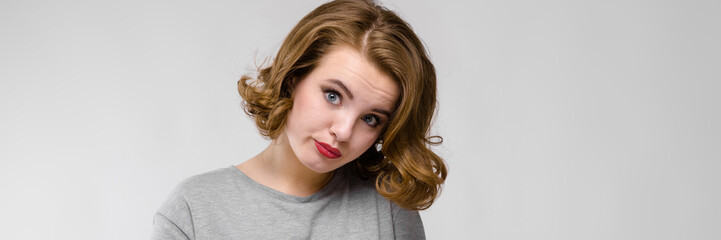 Naklejka premium Charming young girl in a gray T-shirt on a gray background. The girl points a finger at her wrist