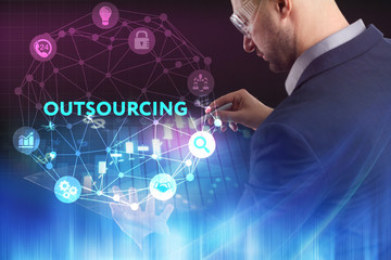 The concept of business, technology, the Internet and the network. A young entrepreneur working on a virtual screen of the future and sees the inscription: Outsourcing