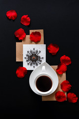 White cup of coffee on a black background in a graphic layout with rose petals with copy space flat lay top view art trend glamor romantic style