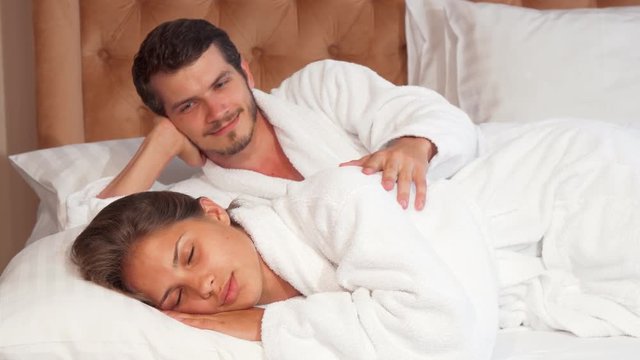 Lovely couple sleeping in their bed together. Handsome young man touching his sleeping wife gently, lying in the bed together. Lovely couple sleeping in their hotel room during vacation. Woman