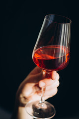 hand holds a glass of fresh red wine on a dark background