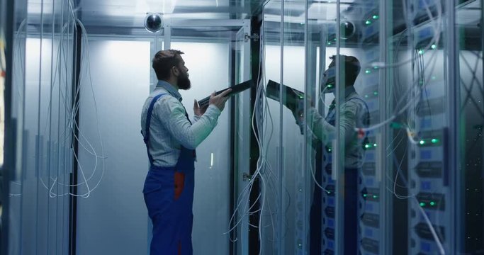 Medium shot of a male technician working in a data center carrying peforming maintenance amongst rows of server racks installing server equipment