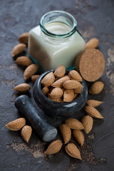 Marble pounder with unpeeled almond nuts and a bottle of almond milk, vertical shot over brown stone background