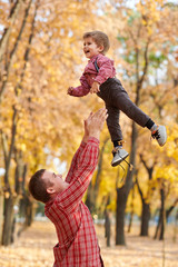 Father throws the boy high up. Father and son are playing and having fun in autumn city park. They posing, smiling, playing. Bright yellow trees.