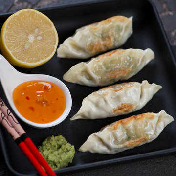 Pan fried korean dumplings with dipping sauces in a cast-iron serving tray, closeup, square shot