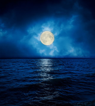 full super moon in dramatic clouds over dark water