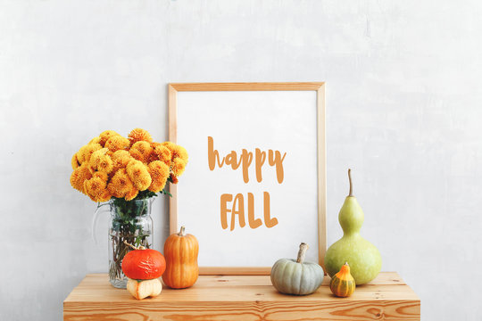 Frame With Text HAPPY FALL, Decorative Pumpkins, Lagenaria Or Bottle Gourd And Vase With Yellow Chrysanthemums Flowers On A Wooden Table On A Background Of Light Gray Walls. Autumn Home Interior Decor