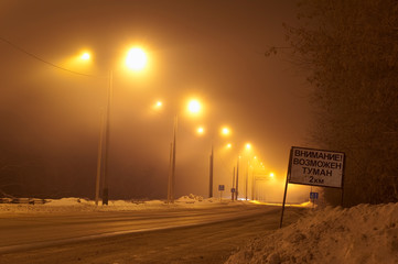 Obraz premium Foggy winter night road. Road sign CAUTION, POSSIBLE FOG