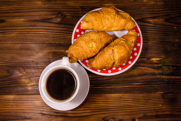 Cup of dark coffee and croissants on wooden table. Top view