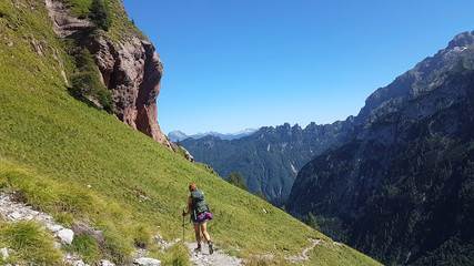 Fototapeta na wymiar Hiker with backpack walking a grass trail on top of a mountain and enjoying valley view during sunny trip in the alps