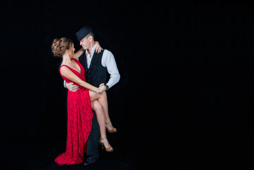 Young beautiful woman in red dress and guy dancing tango on black background in Studio