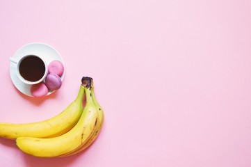 Flat lay food photo. Cup of coffee, macaroons cookies and bunch of bananas on a pink table. Useful snack