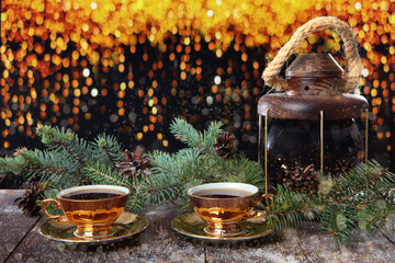 Two cups of coffee with gold color on the background of fir branches. Wooden background and garlands. New year holidays and Valentine's day.