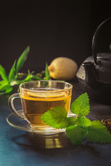 Cup with tea, mint and black teapot on dark background. Closeup. Chinese tea concept.