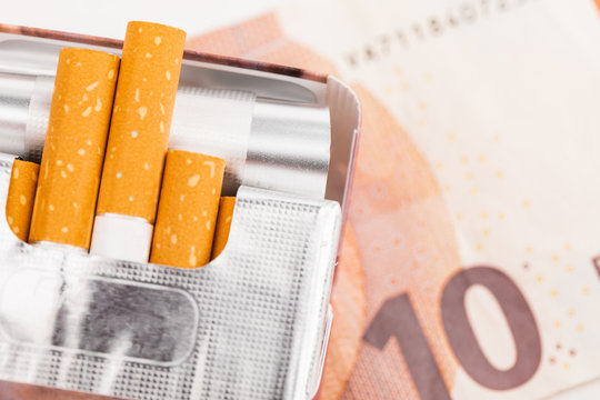 Open pack of cigarettes with yellow filter on the background of Euro banknotes.
