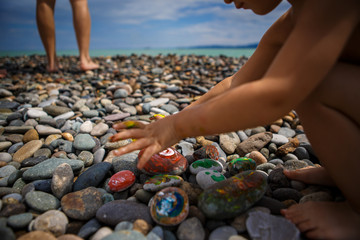 Children's entertainment on a pebble beach-paint stones. Painted with finger paints stones and jars of paint, leisure for the child.